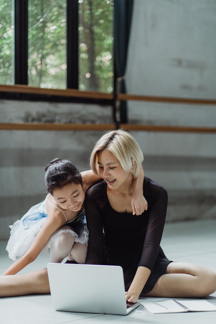A ballet coach and her student in a studio, using a laptop for an online lesson.